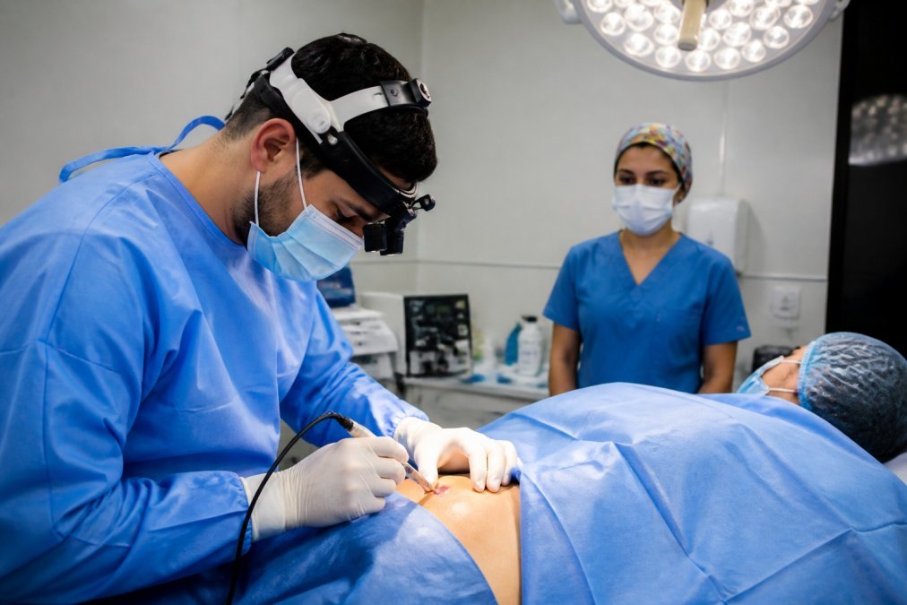 Consultorio médico moderno con equipamiento visible, lámpara quirúrgica encendida, bandeja de instrumentos esterilizados, ambiente clínico limpio y profesional
