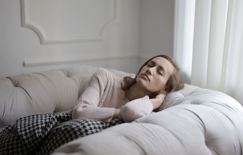 Mujer descansando con los ojos cerrados en un sofá acogedor, ilustrando el manejo del estrés relacionado con los brotes recurrentes de herpes genital.