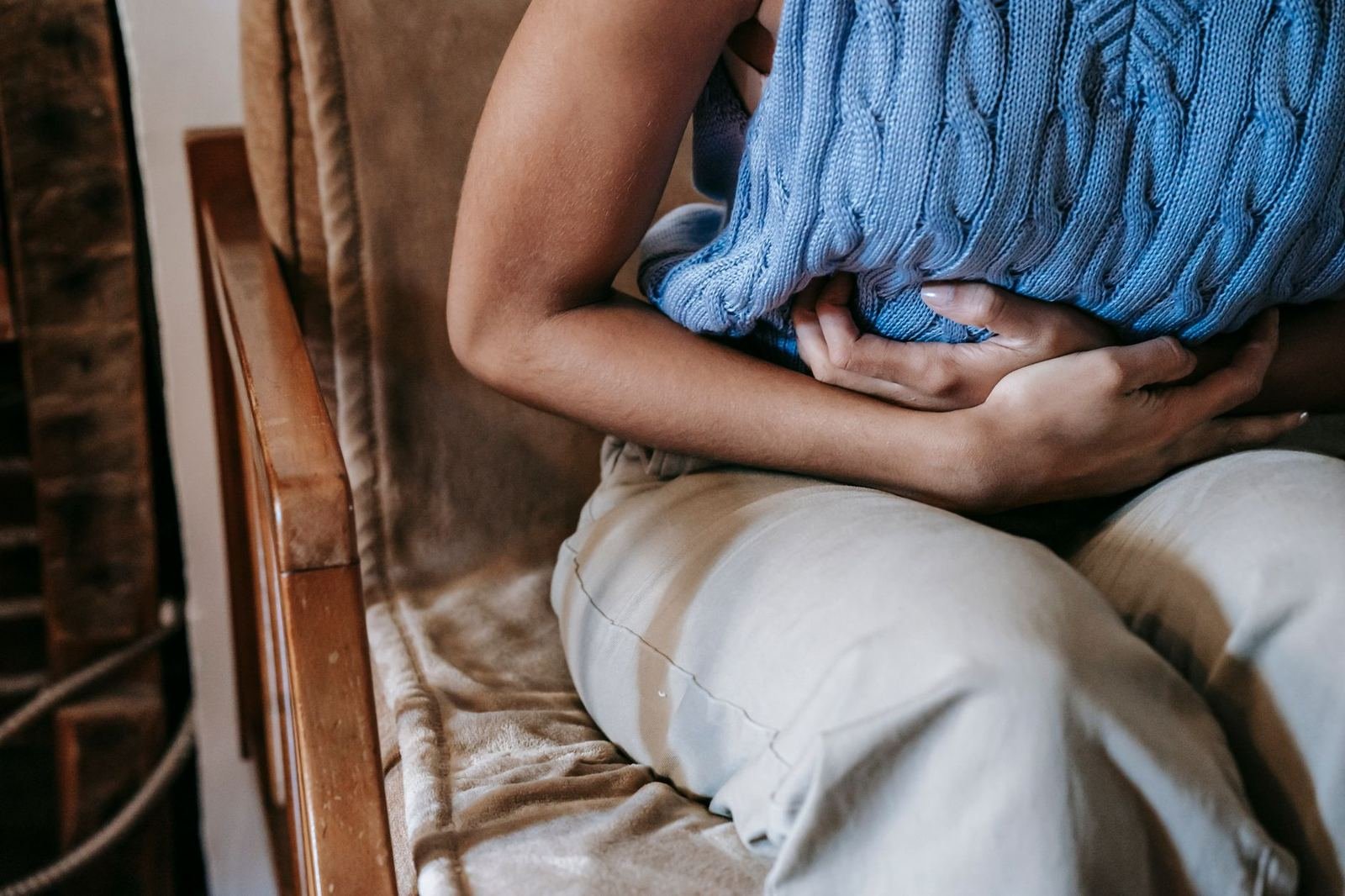 Persona sentada en un sillón con los brazos cruzados sobre el abdomen, sin rostro visible ni texto