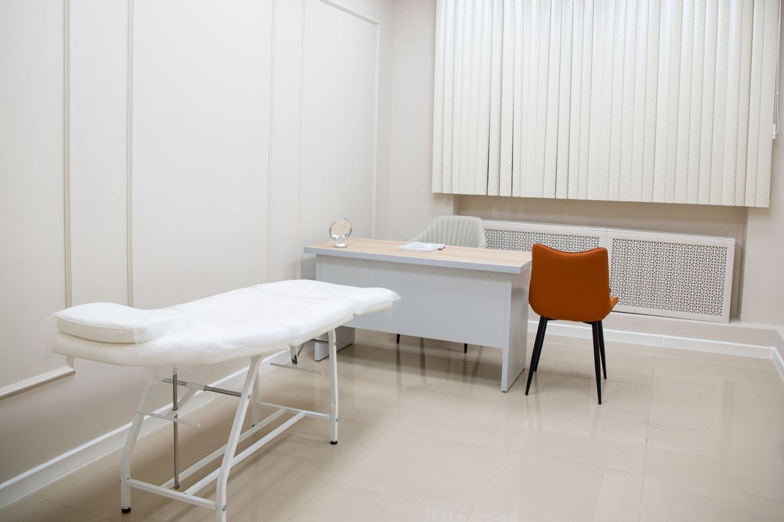 Consultorio médico vacío y luminoso con una camilla blanca, un escritorio y una silla naranja, sin personas ni texto