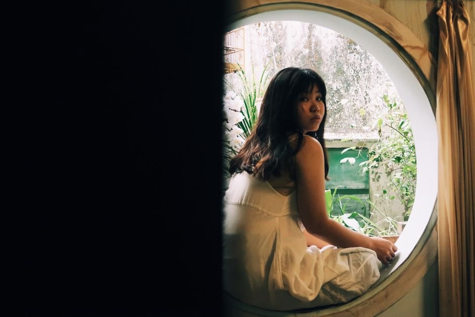 Mujer sentada junto a una ventana circular con luz natural, mirando hacia afuera, en un ambiente tranquilo asociado a bienestar y salud ginecológica