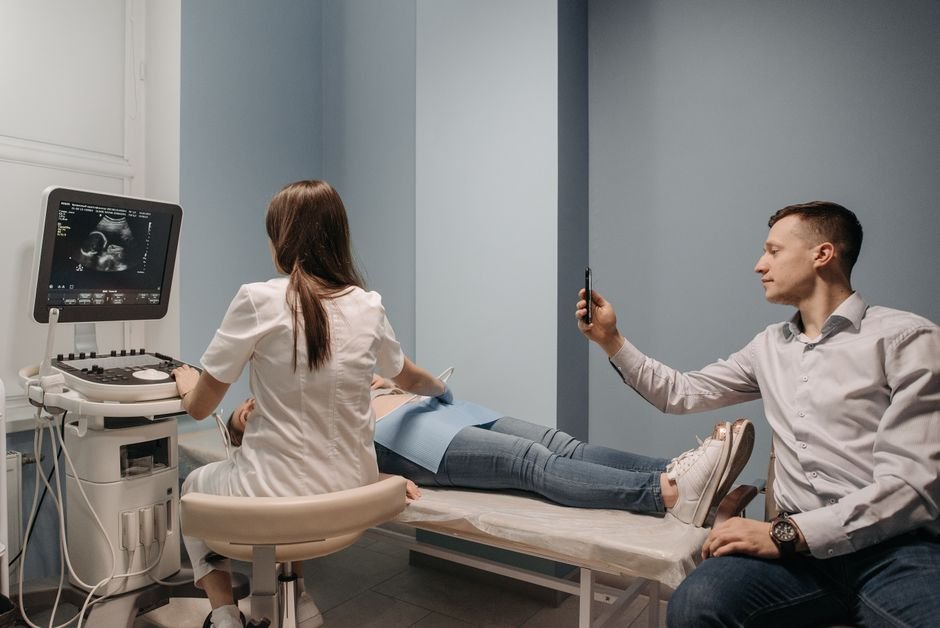 Personal de salud de espaldas realizando un ultrasonido prenatal a una mujer embarazada en un consultorio