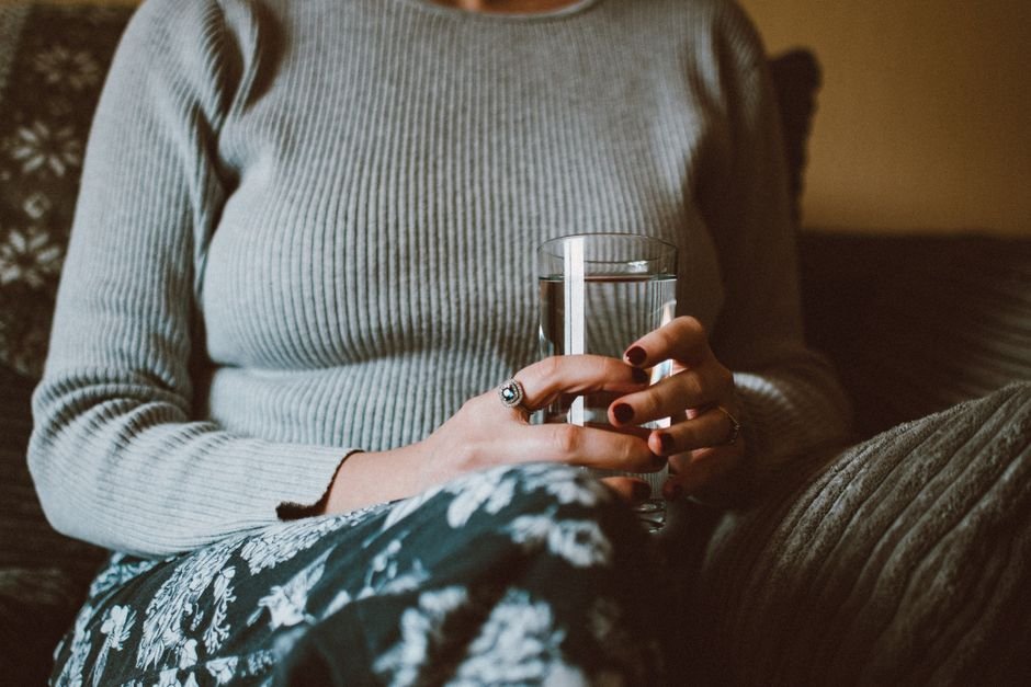 Primer plano de manos sosteniendo un vaso de agua, sin mostrar el rostro, en un ambiente asociado al cuidado de la salud urinaria y vaginal