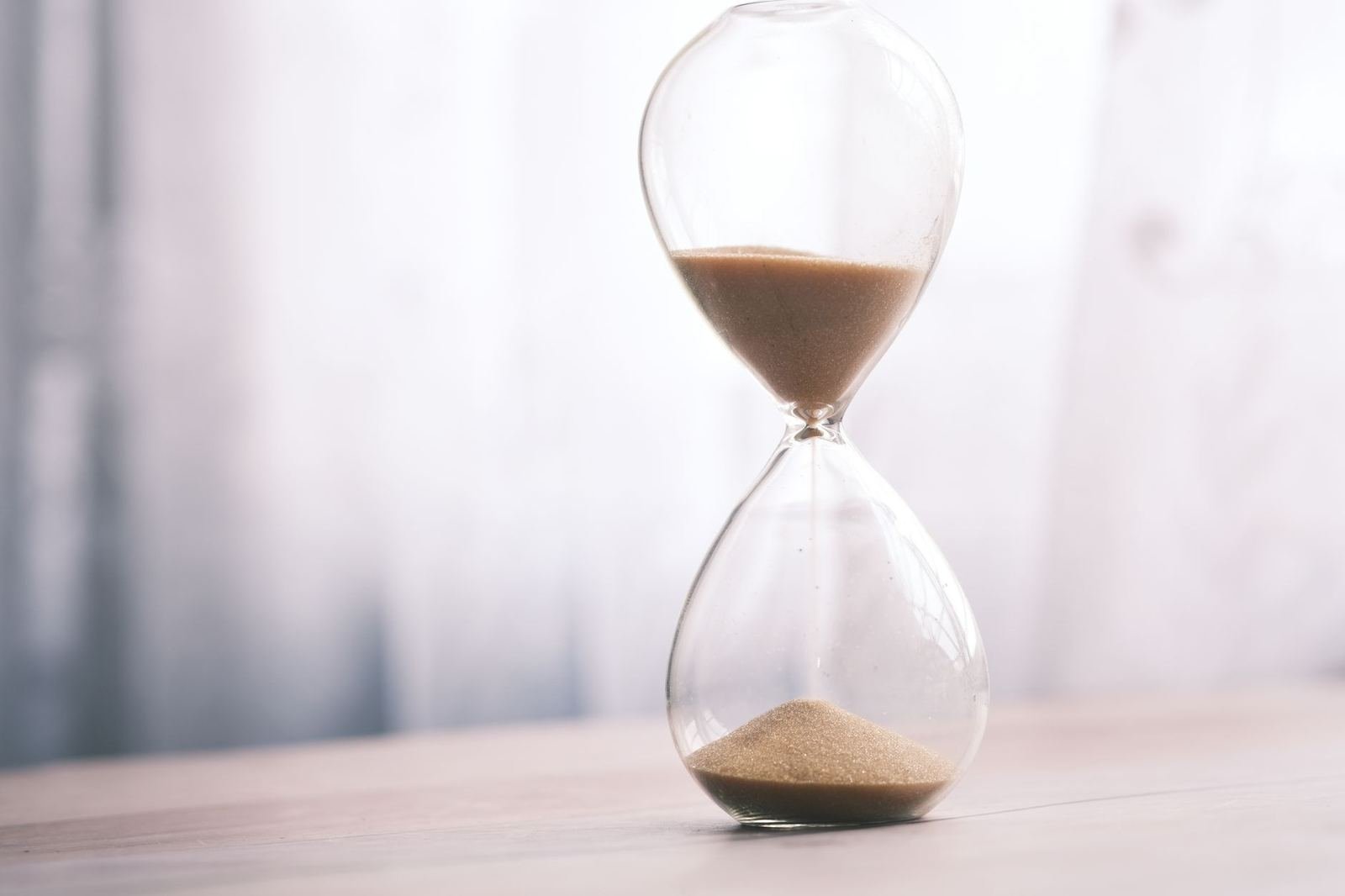 Reloj de arena de vidrio sobre una mesa de madera clara con luz suave, sin personas ni texto