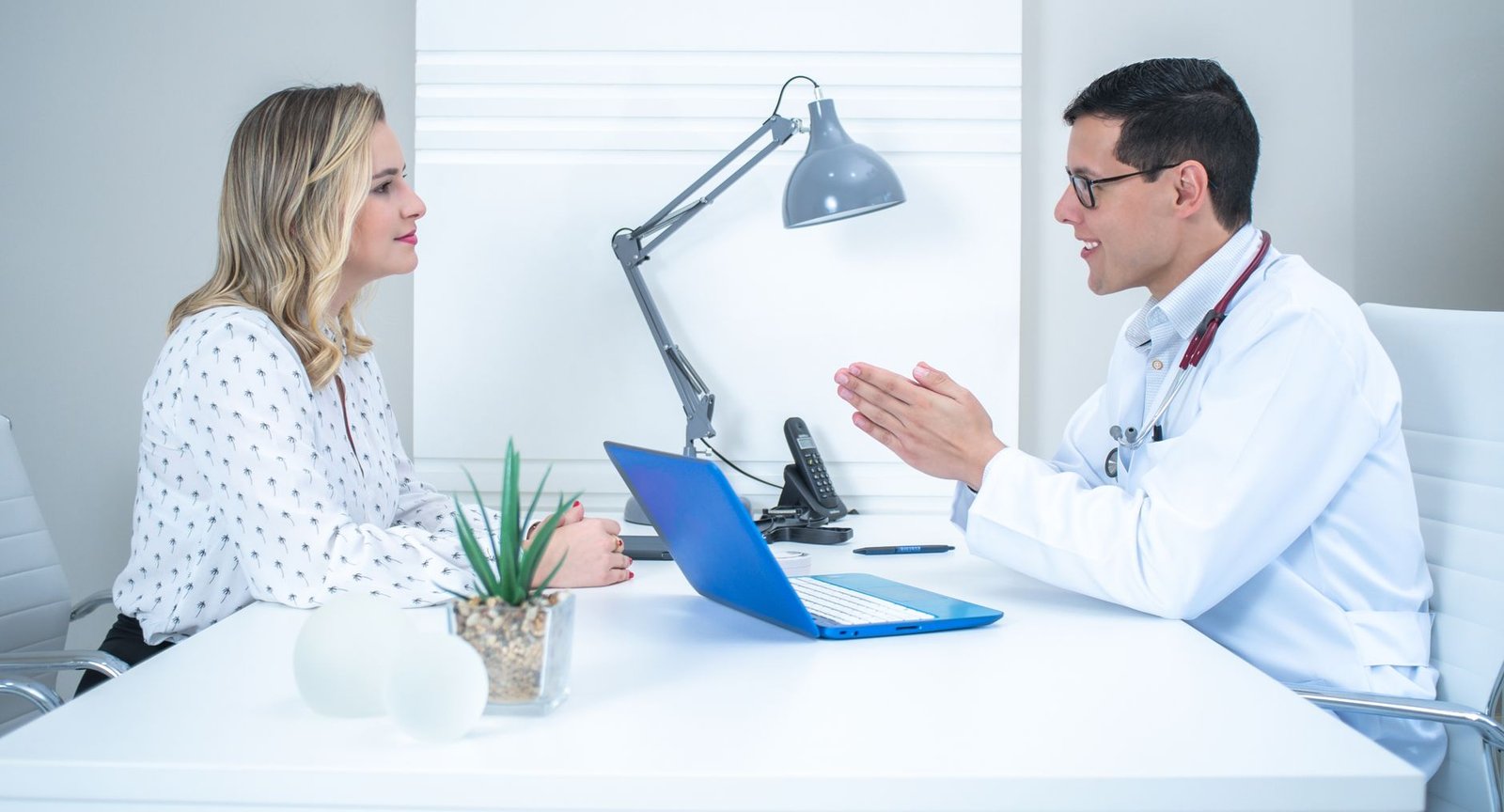 Profesional de la salud conversando de perfil con una paciente en un consultorio médico privado.