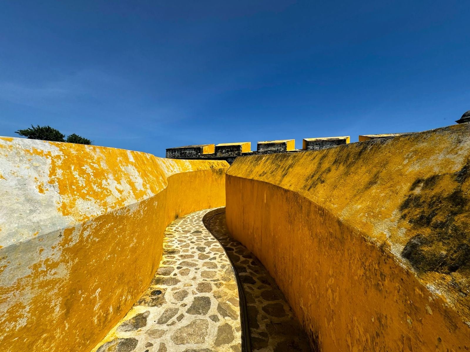Pasillo curvo de piedra entre muros amarillos de una fortaleza colonial bajo un cielo azul intenso, en Campeche, sin personas