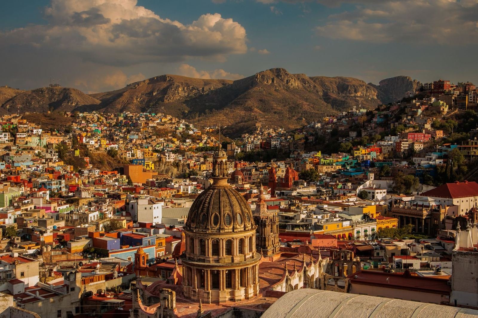 Vista panorámica de la ciudad de Guanajuato con casas de colores, una cúpula antigua y cerros al fondo, sin personas