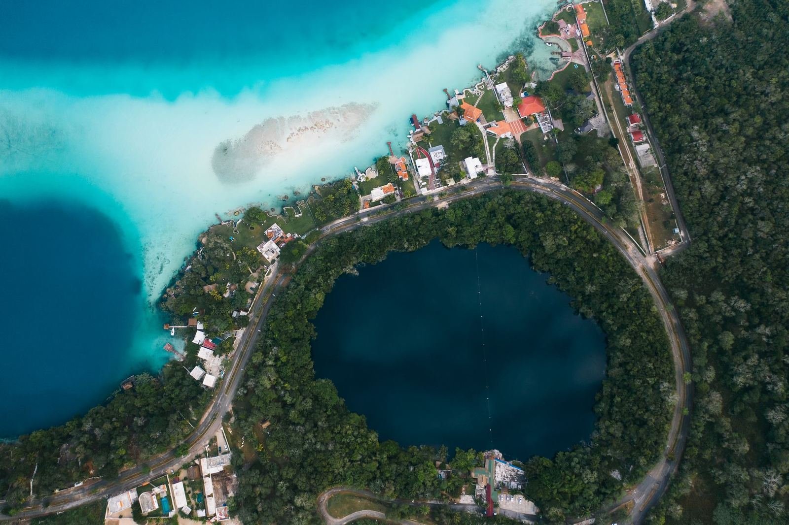 Vista aérea de un cenote circular de agua oscura rodeado de selva junto a la laguna turquesa de Bacalar, sin personas