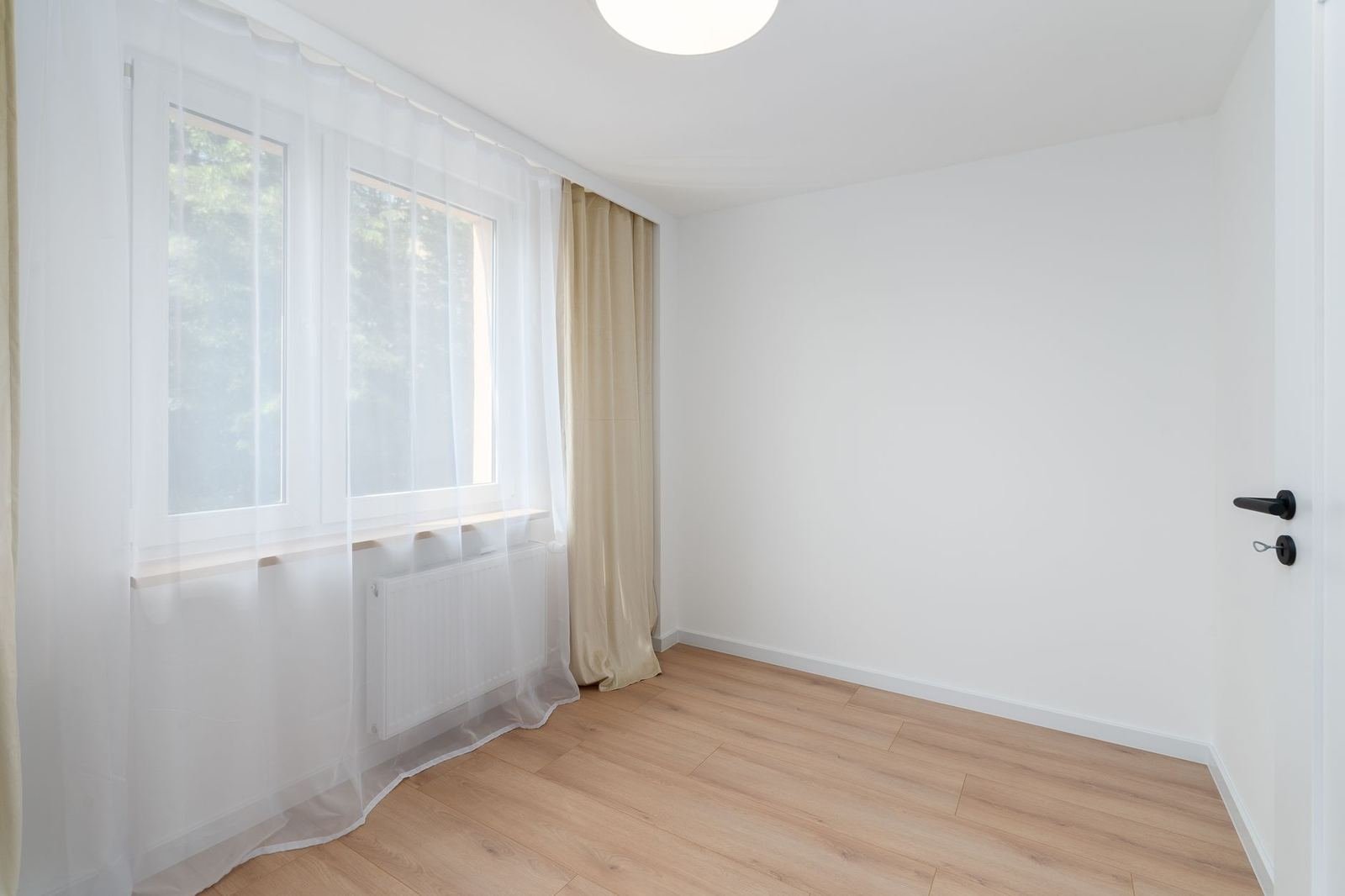 Habitación luminosa y vacía con cortinas blancas translúcidas junto a una ventana, sin personas ni texto