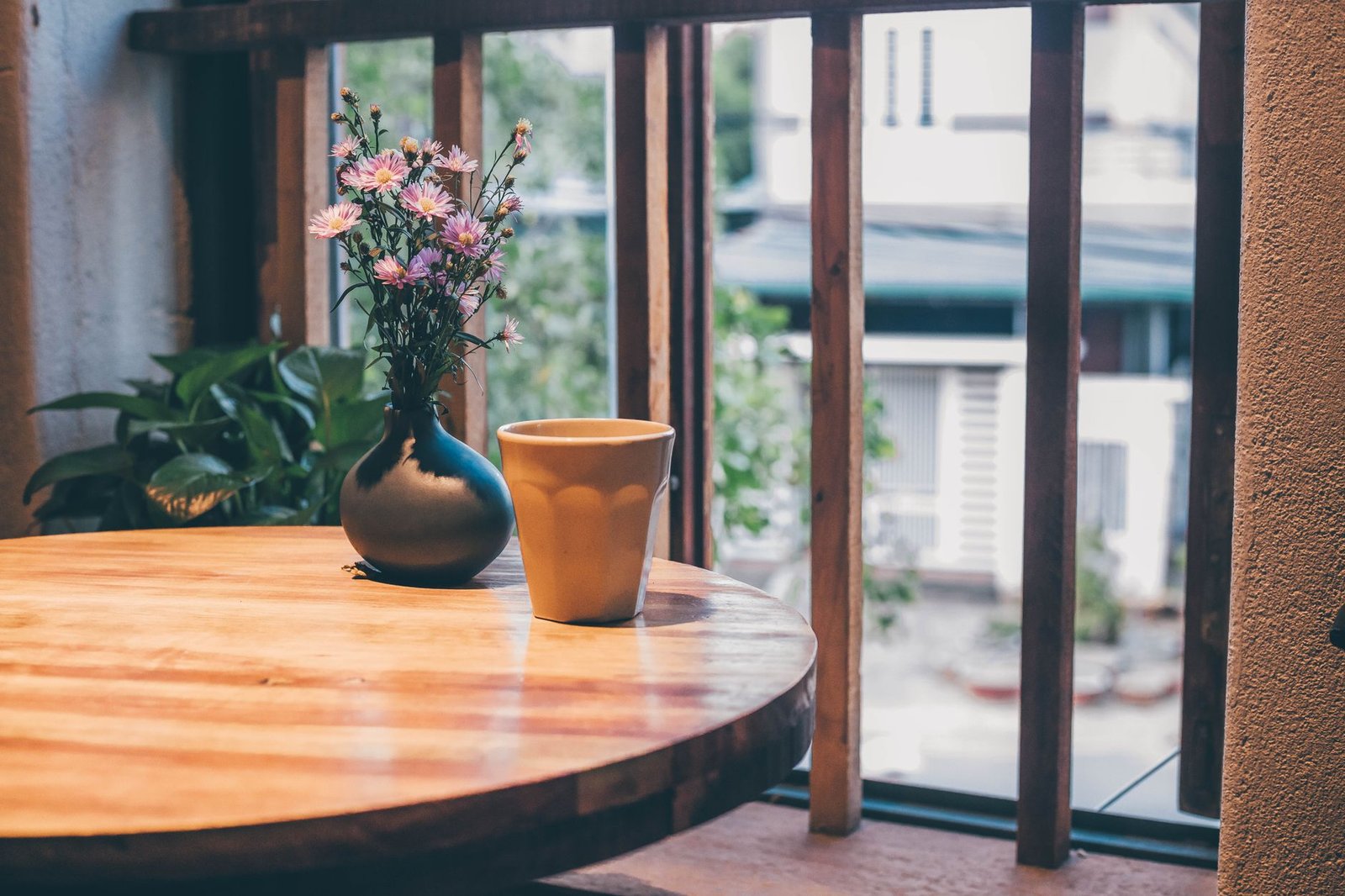 Una taza y un pequeño florero sobre una mesa de madera junto a una ventana con luz de la tarde, sin personas
