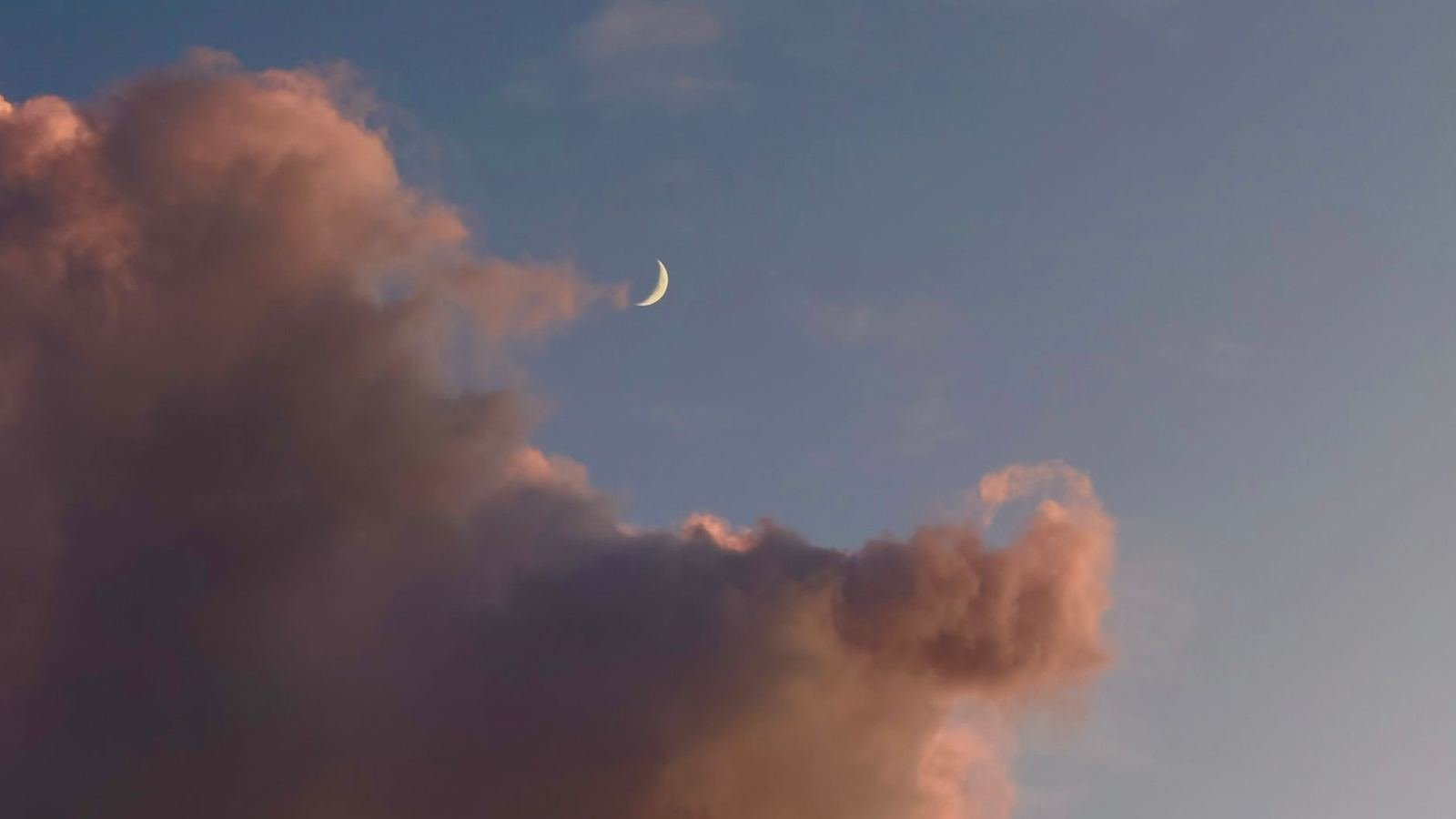Una luna creciente delgada entre nubes rosadas al atardecer, sin personas ni texto