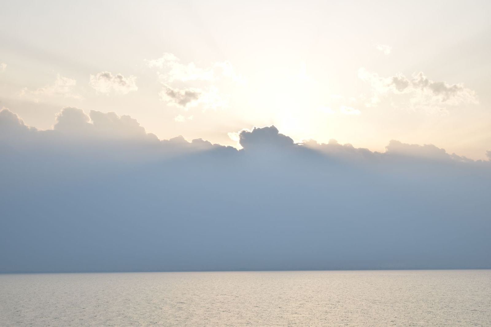 Rayos de sol atravesando nubes sobre un mar en calma, sin personas ni texto