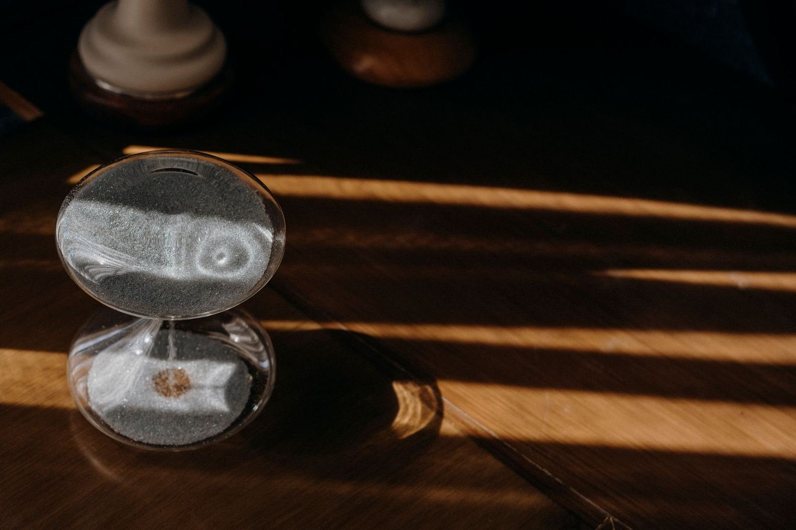 Reloj de arena sobre una mesa de madera con luz de la mañana entrando en franjas, sin personas ni texto