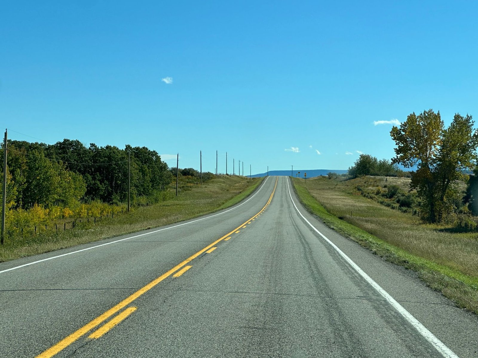Una carretera larga y recta que se extiende hacia el horizonte entre campos verdes, sin personas ni vehículos