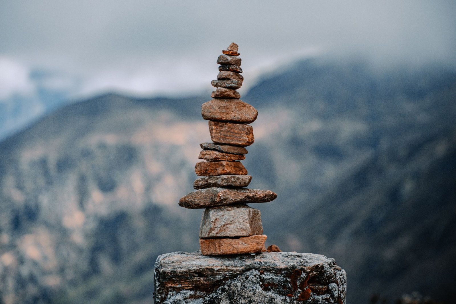 Una torre de piedras balanceadas cuidadosamente sobre una roca, con montañas neblinosas de fondo, sin personas