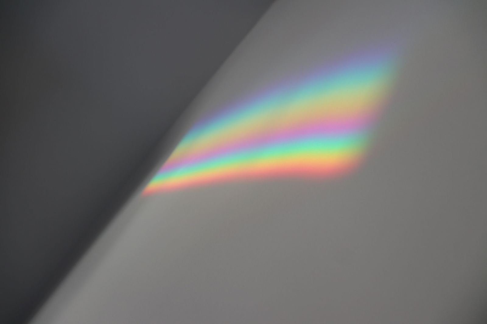 Luz que forma un arcoíris suave sobre una pared gris lisa, sin personas ni texto