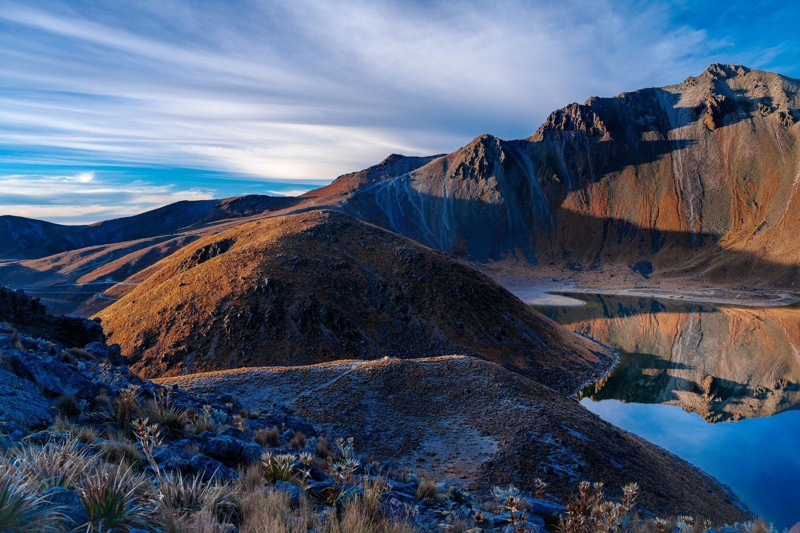 Un lago de cráter entre montañas del Nevado de Toluca al amanecer, con cielo azul y nubes, sin personas ni texto