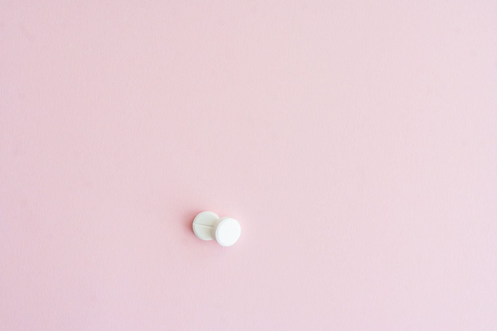 Tabletas blancas sobre una superficie rosa pálido, vista cenital, sin personas ni texto