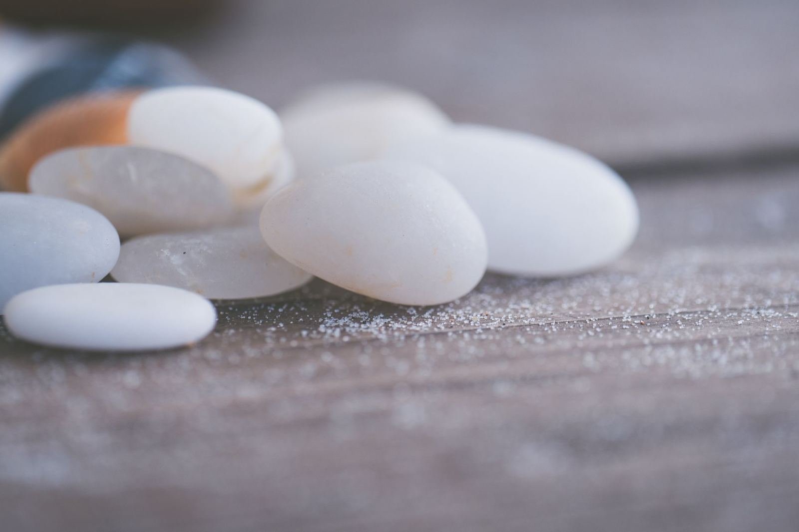 Piedras blancas lisas y redondeadas sobre una superficie de madera con arena fina, luz suave, sin personas ni texto