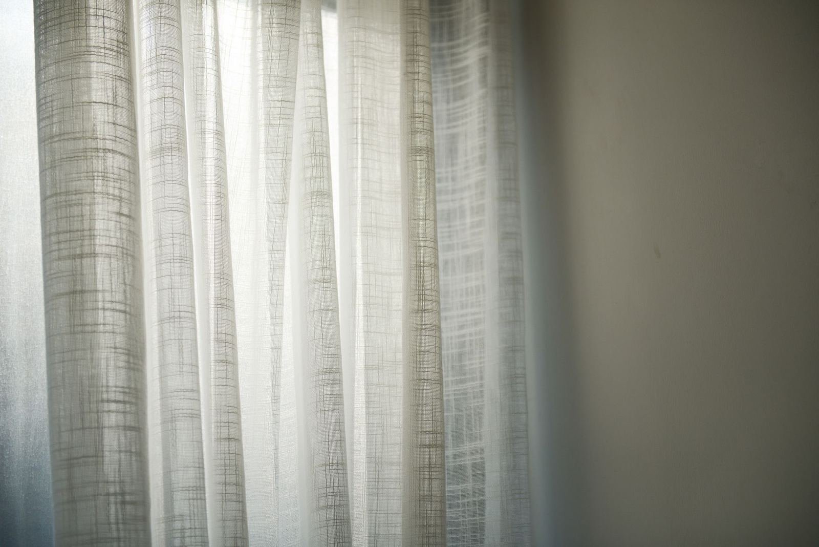 Cortinas de lino blanco con luz de día filtrándose junto a una pared lisa, sin personas ni texto